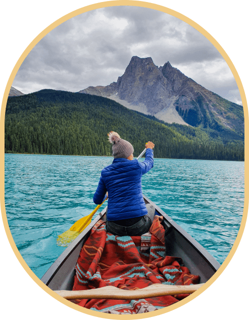 Person canoeing on turquoise lake, mountain backdrop.