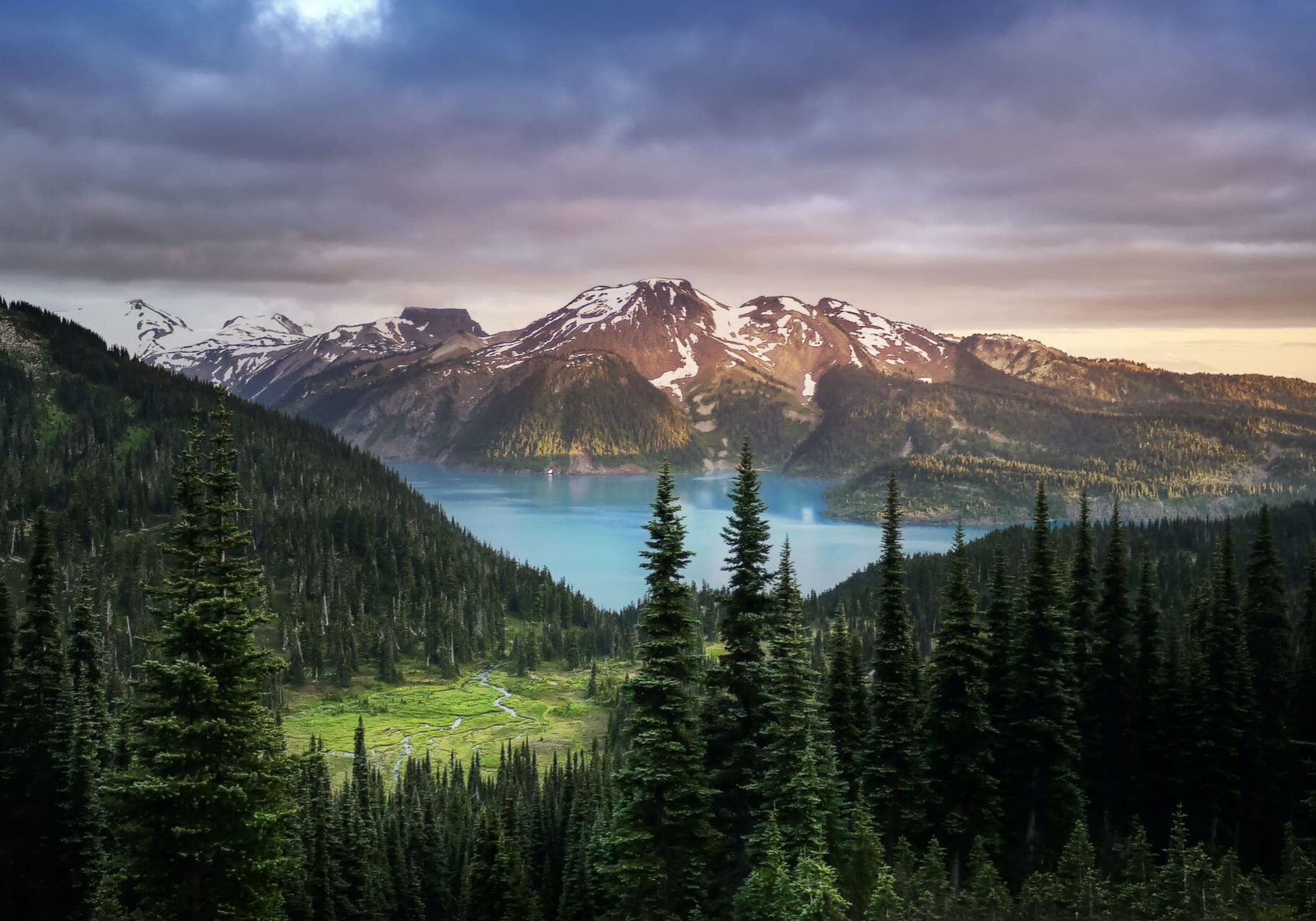 Mountain lake with forest and cloudy sky.